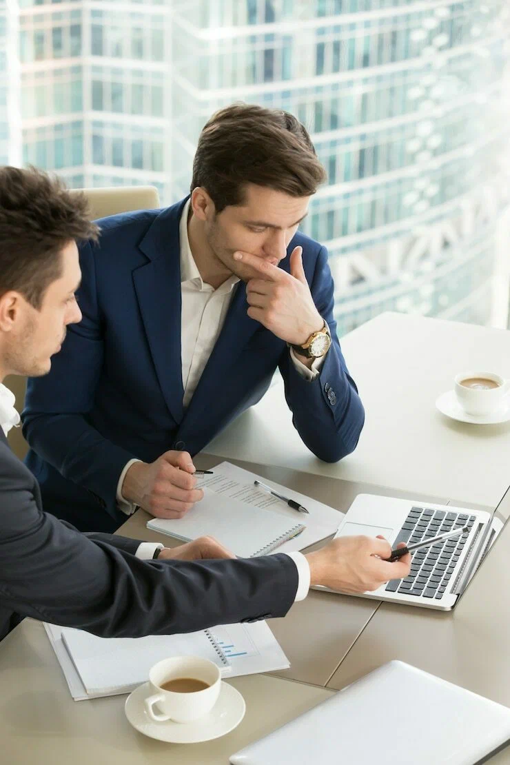 Businessmen reviewing data on a laptop while discussing funding options for a business expansion loan.