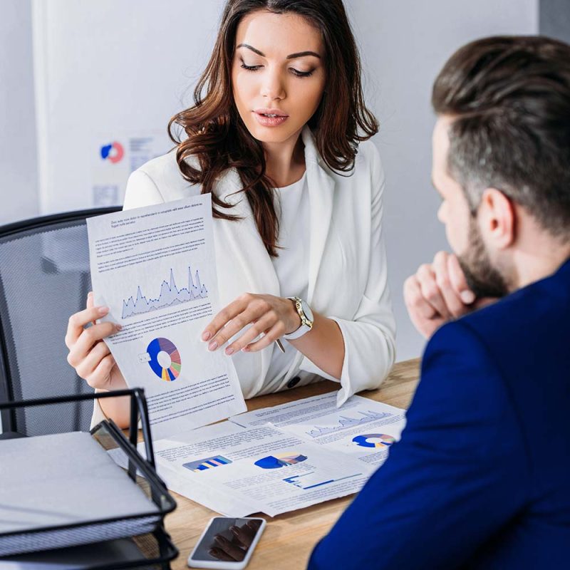 Financial advisor at Chasewood Financial discusses investment charts and reports with a client during a strategy meeting.
