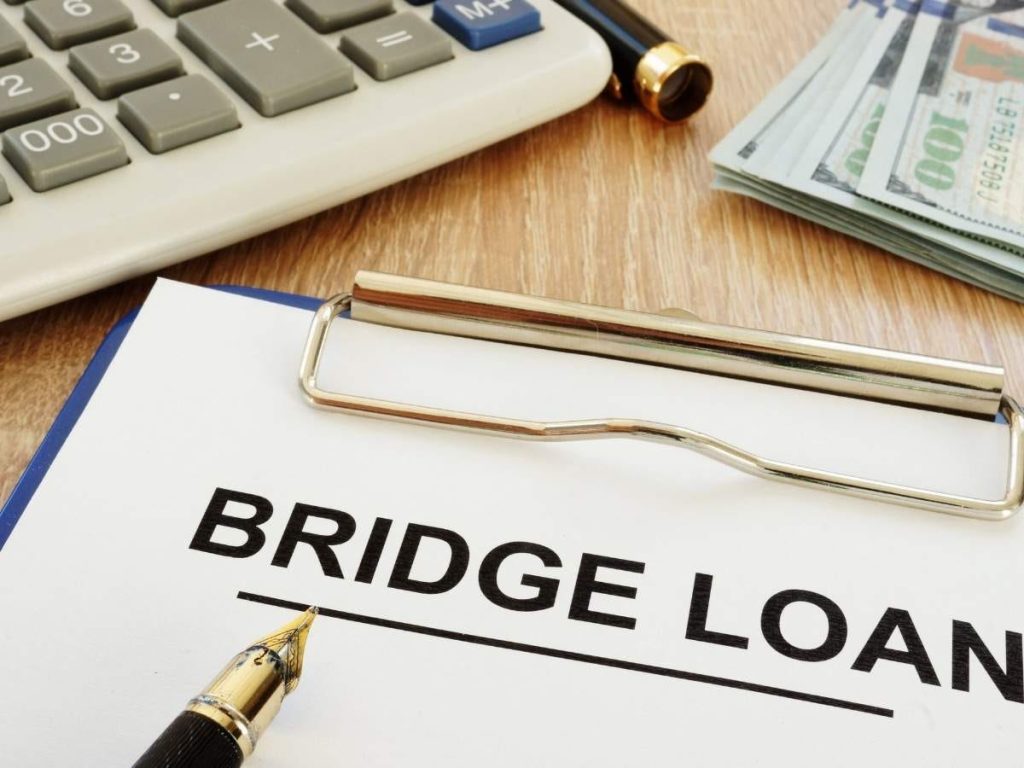 A document titled "BRIDGE LOAN" with a pen, calculator, and stack of cash on a wooden surface.