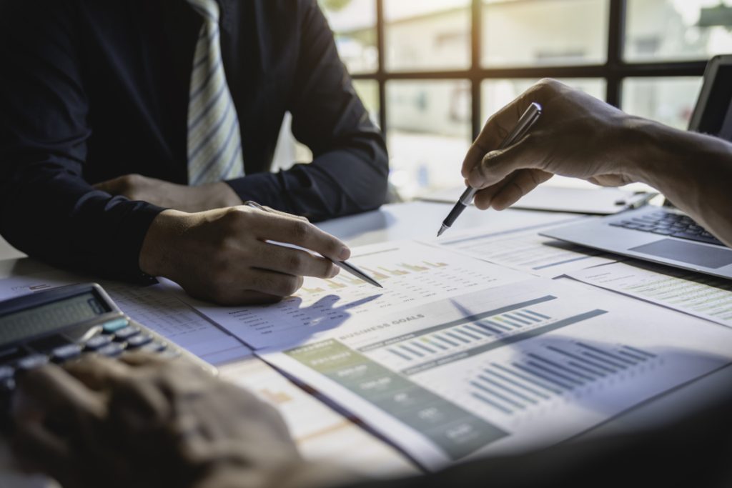 Two professionals reviewing financial charts and graphs on paper during a meeting, discussing data and business goals.
