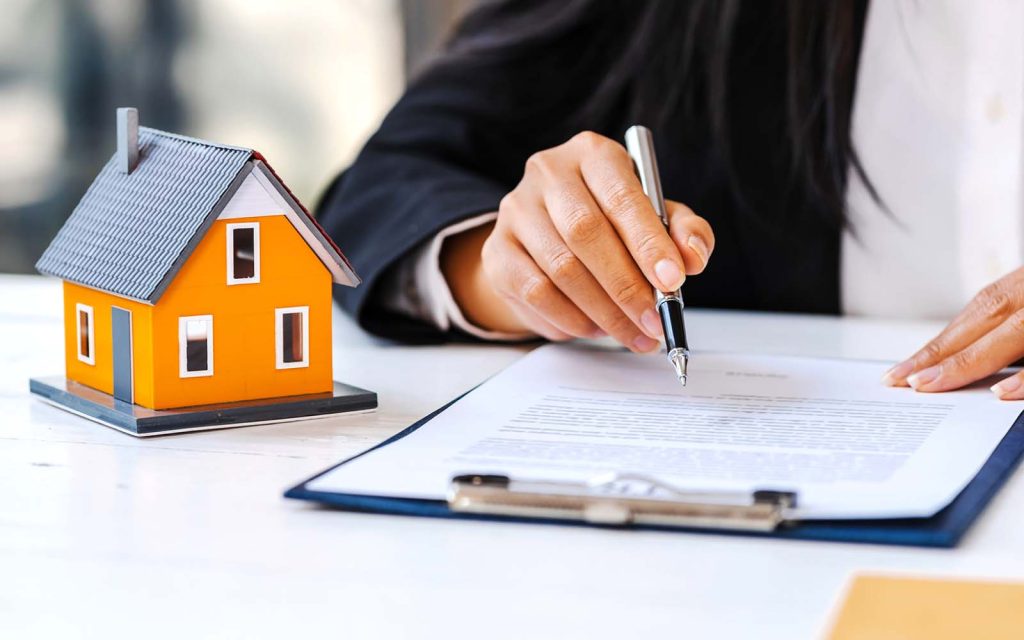 A person signing a contract with a model house and a pen on the table.