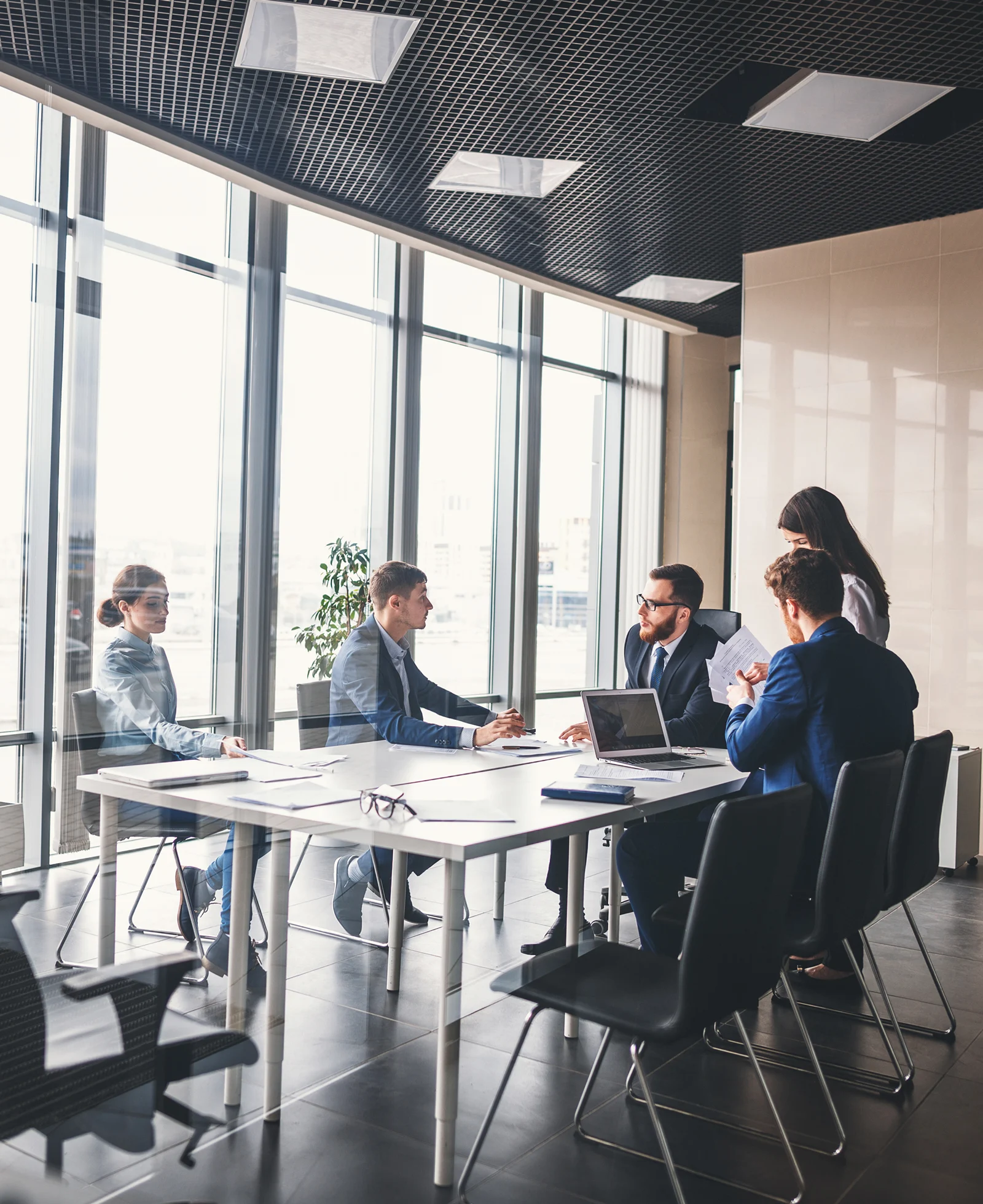 A group of professionals having a meeting around a table in a modern office, with one person standing and others seated.